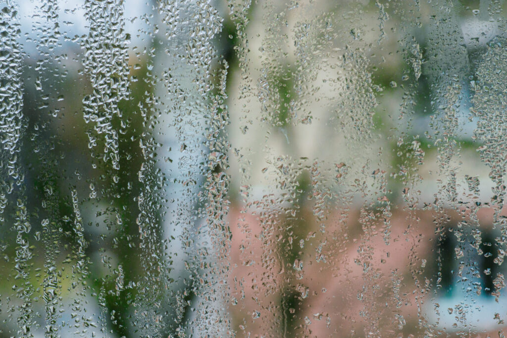 water droplets cling to window in perfect spheres. Steamy window collects condensation in slow-growing droplets. wet window glass abstract background. condensation on glass of apartment